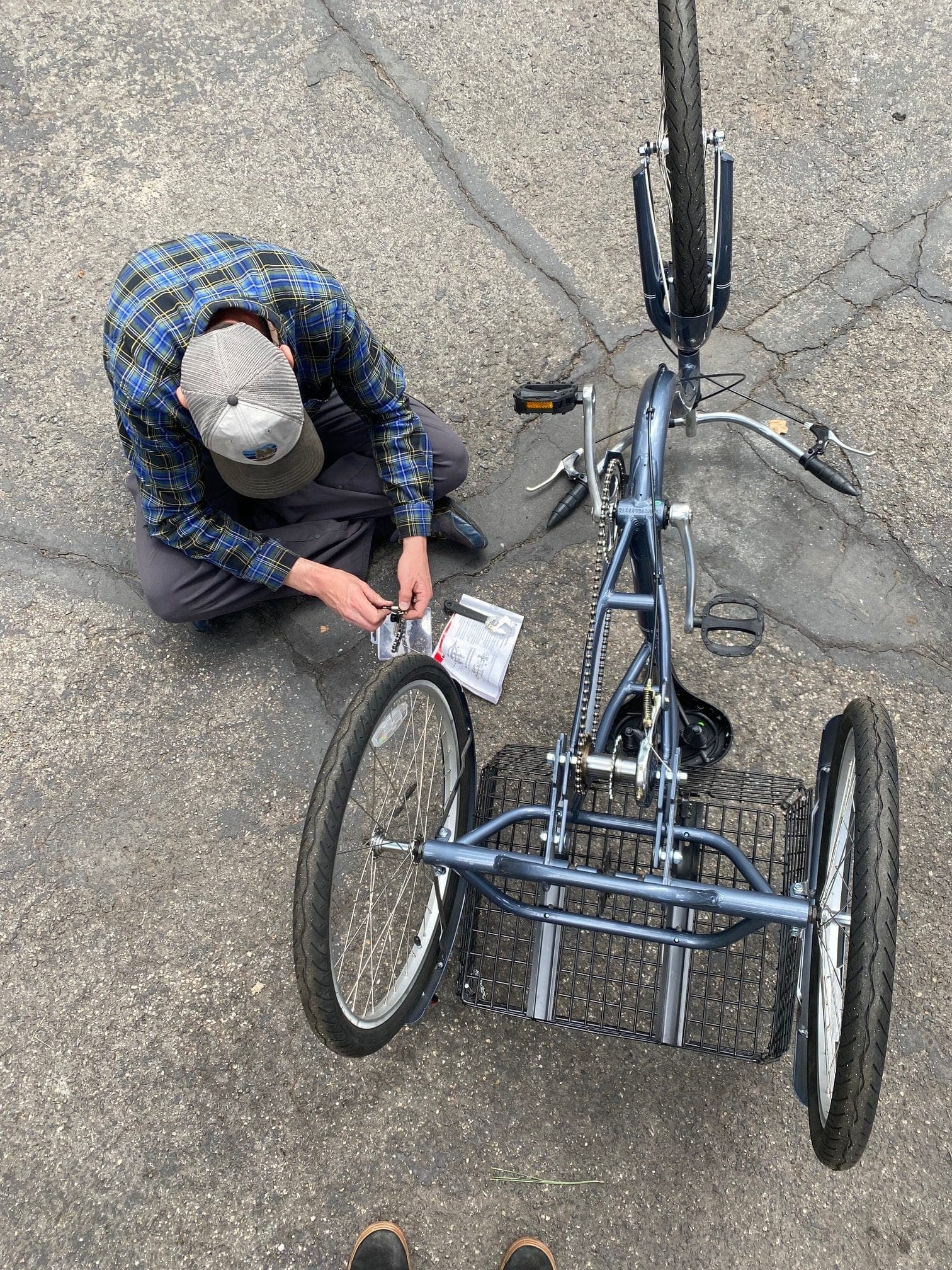 A volunteer kneeling on the pavement to assemble an adult tricycle